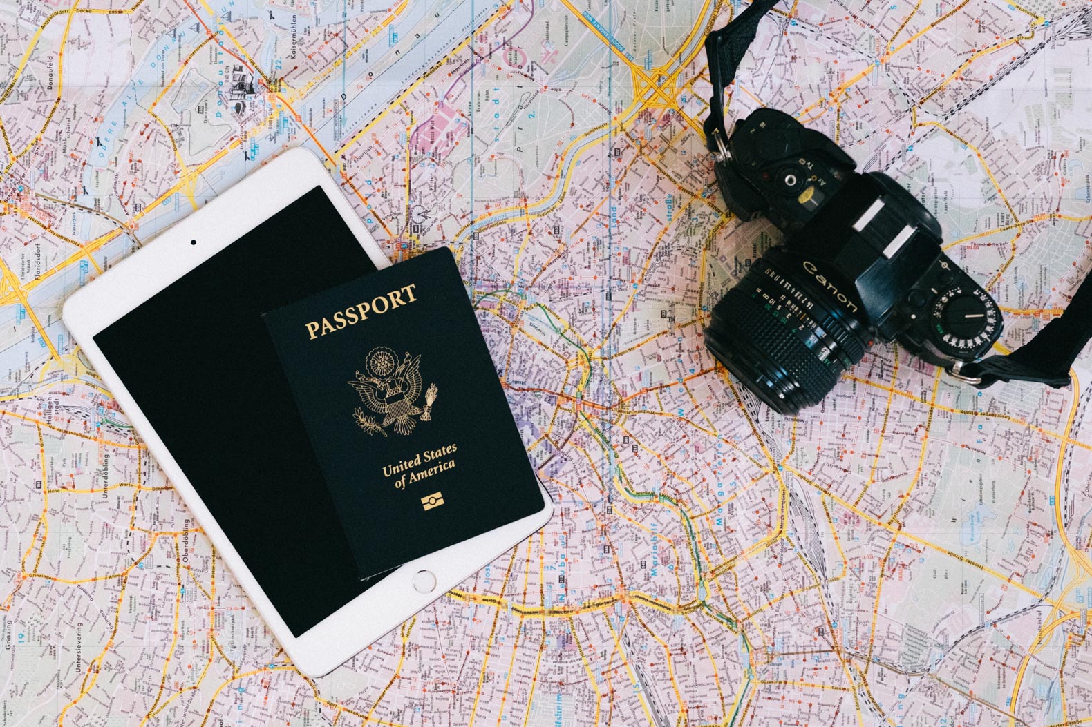 Passport, film camera, and an ipad on a map